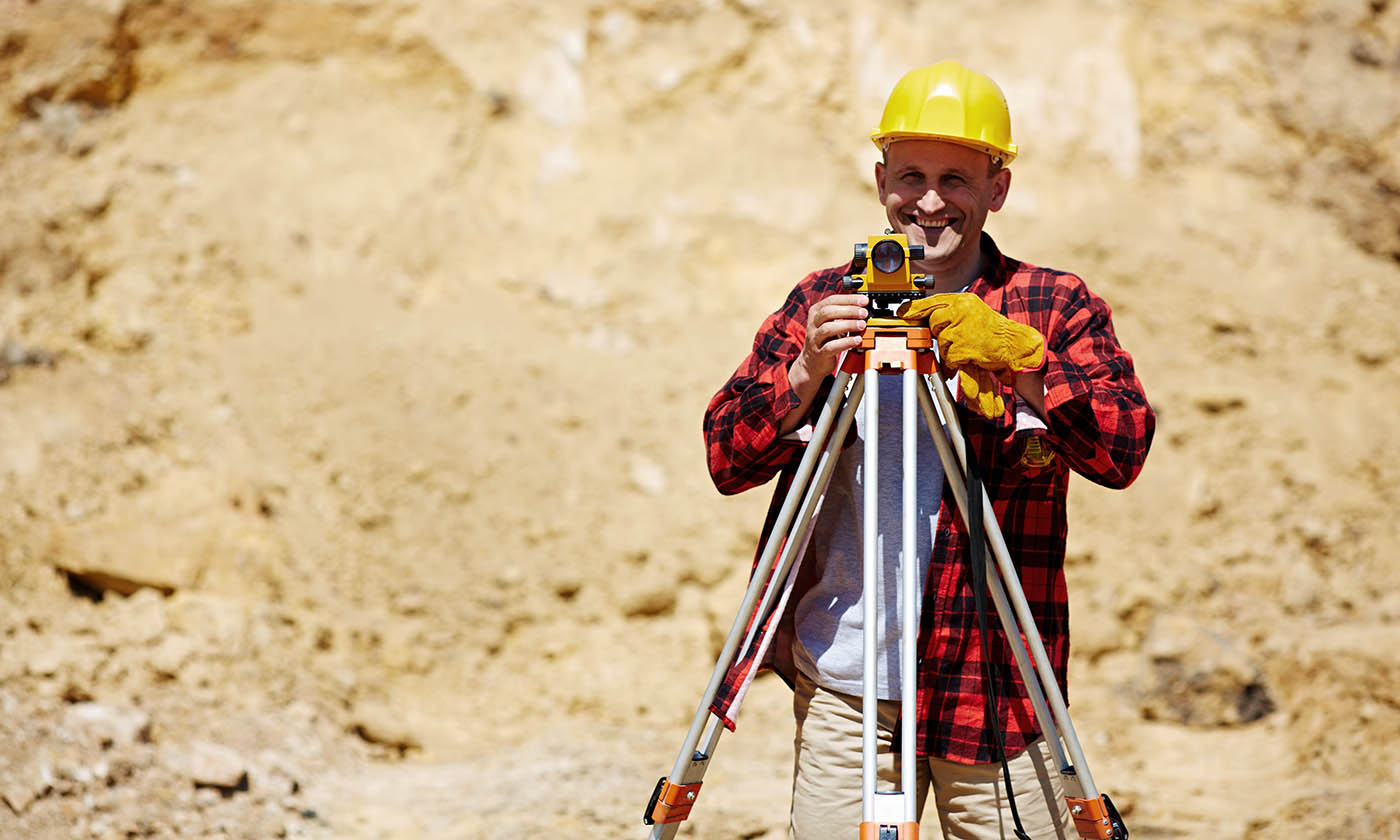 Smiling construction worker in helmet standing with theodolite